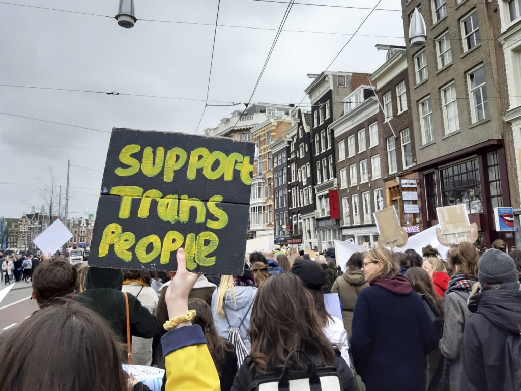 foto van demonstratie waarbij iemand boordje vasthoud met: support trans people erop