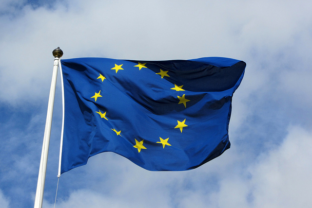 Foto van de Europese vlag, een blauwe vlag met een cirkel van gele sterren, tegen een blauwe lucht met wolken.