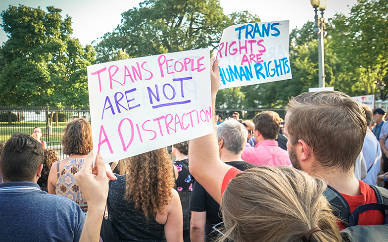 Foto van een transrights march met mensen vanaf de achterkant en borden met de tekst "Trans People Are Not A Distraction" en "Trans Rights Are Human Rights"