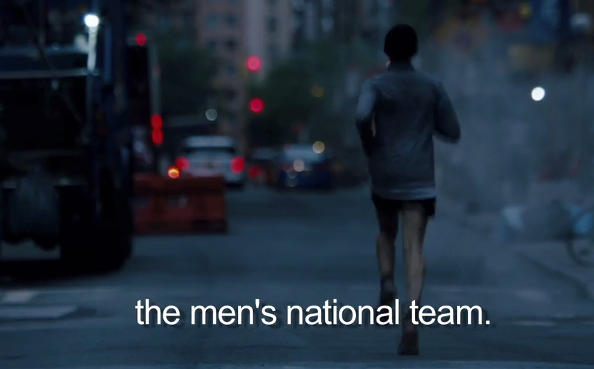 Donkere foto van iemand van achteren die aan het rennen is op straat, je ziet vaag op de achtergrond auto's en verkeerslichten. Over de foto staat de tekst: "the men's national team."