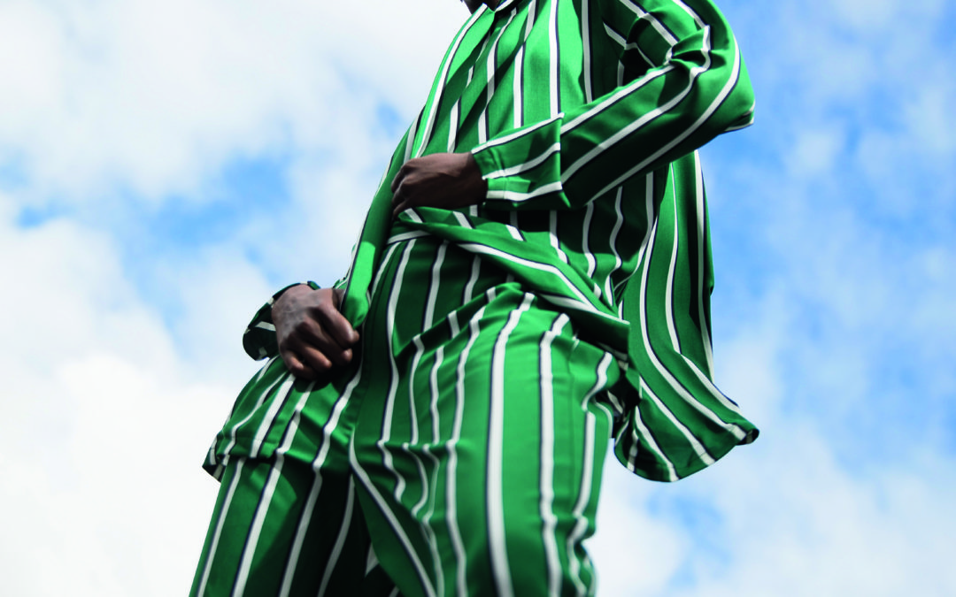 Foto van de romp van een persoon met groen/wit gestreept pak tegen een blauwe lucht