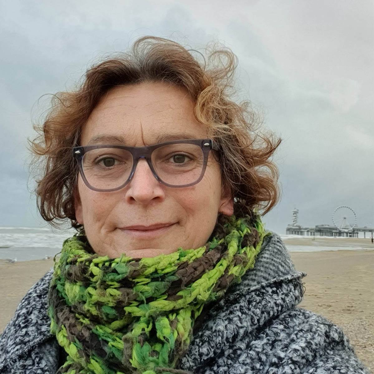 Portret van Willemijn op het strand. Ze draagt een bril en groene sjaal.