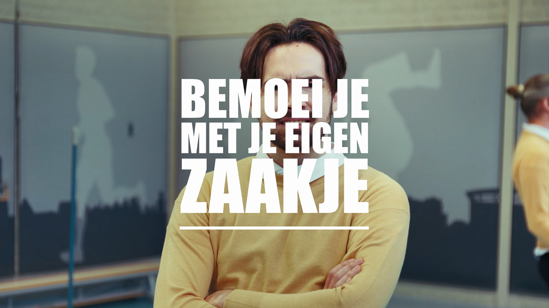 Een persoon in een gele trui staat met gekruiste armen. Er is een wazige persoon op de achtergrond. Tekst in beeld: Bemoei je met je eigen zaakje. De ruimte heeft grijsblauwe wanden met witte silhouetten.