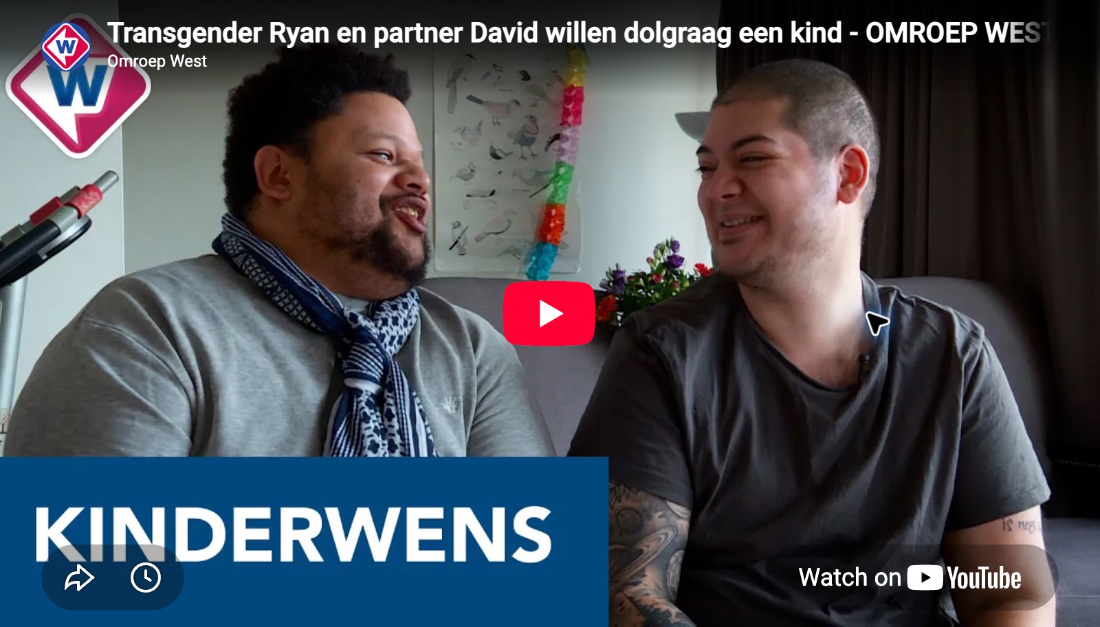 Twee partners zitten naast elkaar op een bank en lachen naar elkaar. Achter hen bloemen en een poster aan de muur. Onderaan een blauwe balk met groot woord KINDERWENS. In het midden een rode speelknop en rechtsonder het YouTube-logo.