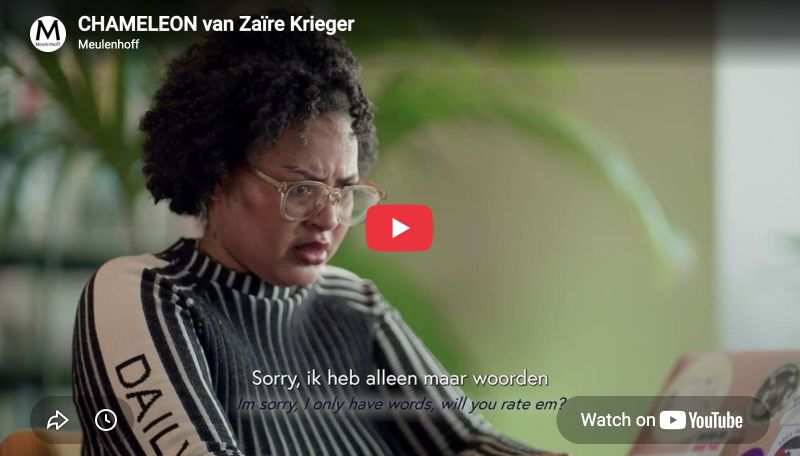 Persoon met krullend haar en bril zit voor een laptop, draagt een gestreepte trui met tekst op de mouw. Rode YouTube-afspeelknop in het midden. Ondertitel: Sorry, ik heb alleen maar woorden. Vage groene planten op de achtergrond.